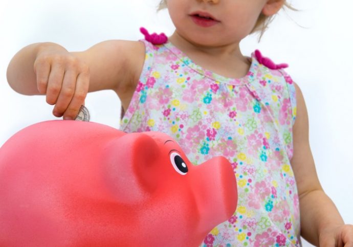 Two-year old girl throwing money into piggy bank. Shallow depth of field.