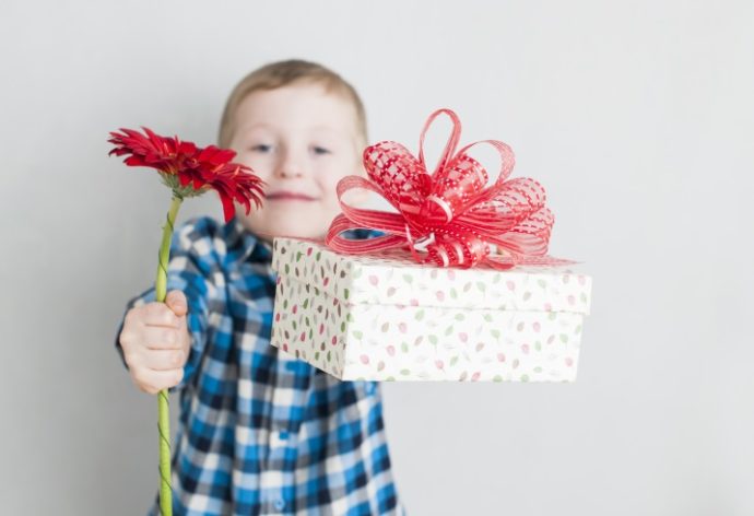 Happy cheerful little boy with red flower and gift box in a banner