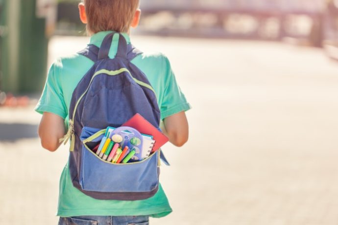 Schoolboy with full backpack go to school. Back view.