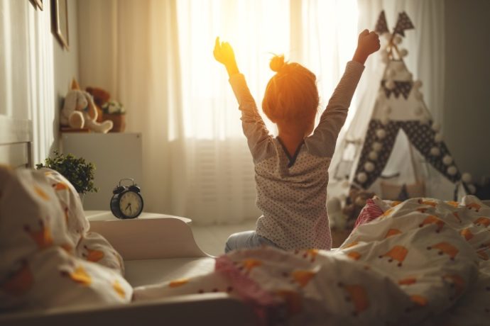 child girl wakes up in morning in bed and stretches by window