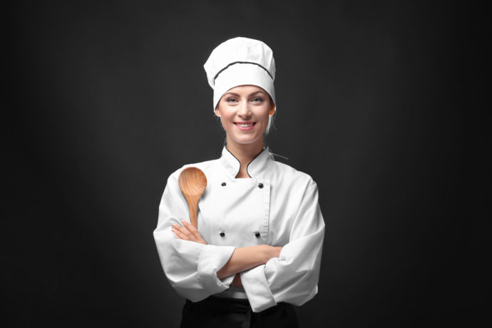 Portrait of female chef with wooden spoon on dark background