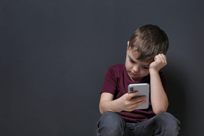 Sad little boy with mobile phone on black background, space for text
