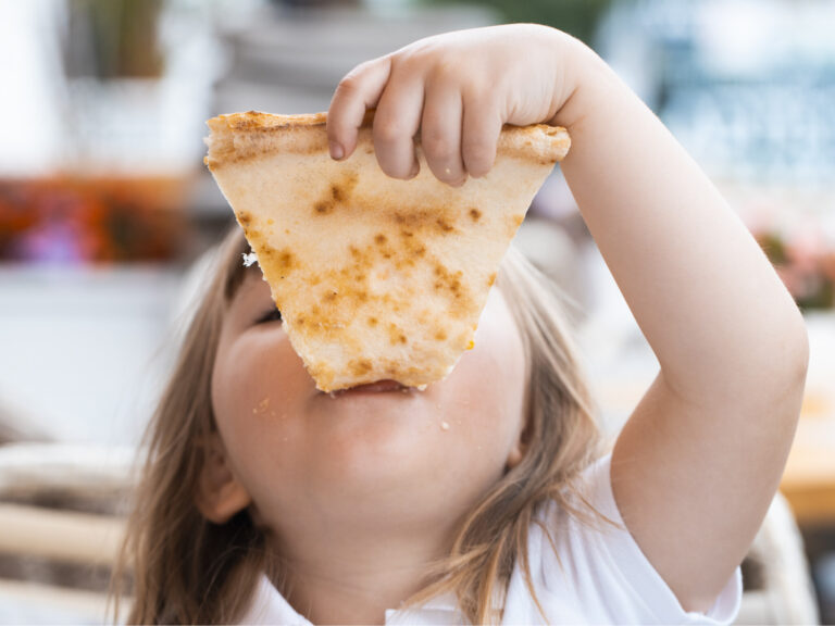 A young girl with plaits is eating a piece of pizza