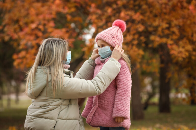 Mother and daughter in medical masks outdoors on autumn day. Protective measures during coronavirus quarantine