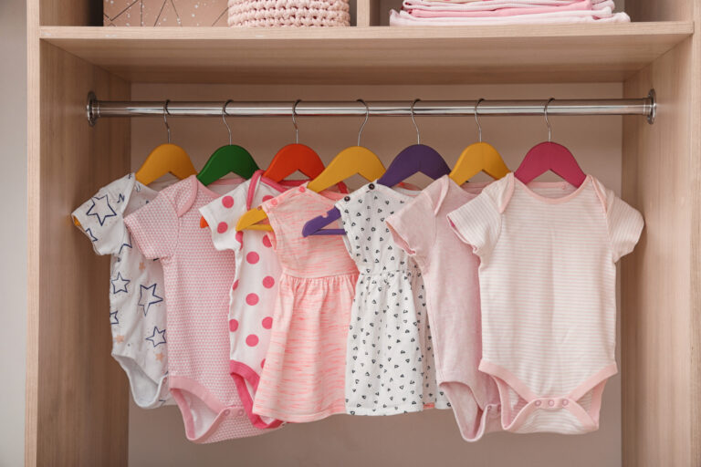 Hangers with baby clothes on rack in wardrobe