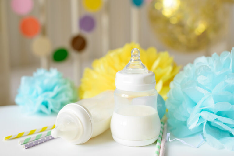 Baby bottle with breast milk, various festive paper decor in front of baby bed. It's a boy or baby birthday celebration concept. Baby shower concept.