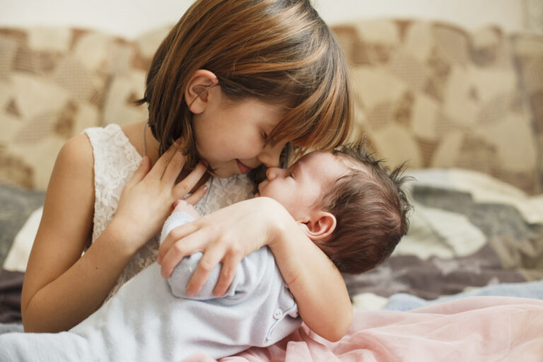 Little sister hugging her newborn brother. Toddler kid meeting new sibling. Cute girl and new born baby boy relax in a home bedroom. Family with children at home.