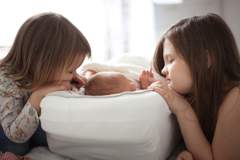 sisters gently watch and hug newborn, baby is sleeping in a cocoon. Real bedroom and lifestyle. The concept of large family and sibling relationship. Three children