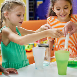 Kids doing chemical experiment at entertainment center. Flasks with colorful liquid on table. Childrens party entertainment.
