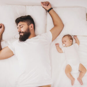 Top view. Bearded Father Sleeps with Baby in Bed. Little Newborn Child in White Bed. Parenthood Concepts. Love and Happiness. Taking Care of New Life. Family, Love, Happiness Concepts.