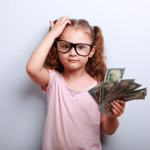 Small professor in eye glasses scratching head, holding money and thinking how earring more. Kid have an big idea. Emotional portrait on blue background with empty copy space