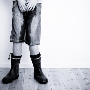 Legs of teenager in short jeans pants wet with water or urine standing on hardwood floor with copy space on wall